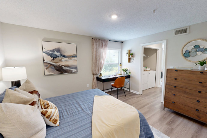 Beige apartment bedroom furnished with a bed, nightstands, wall art, and an area rug
